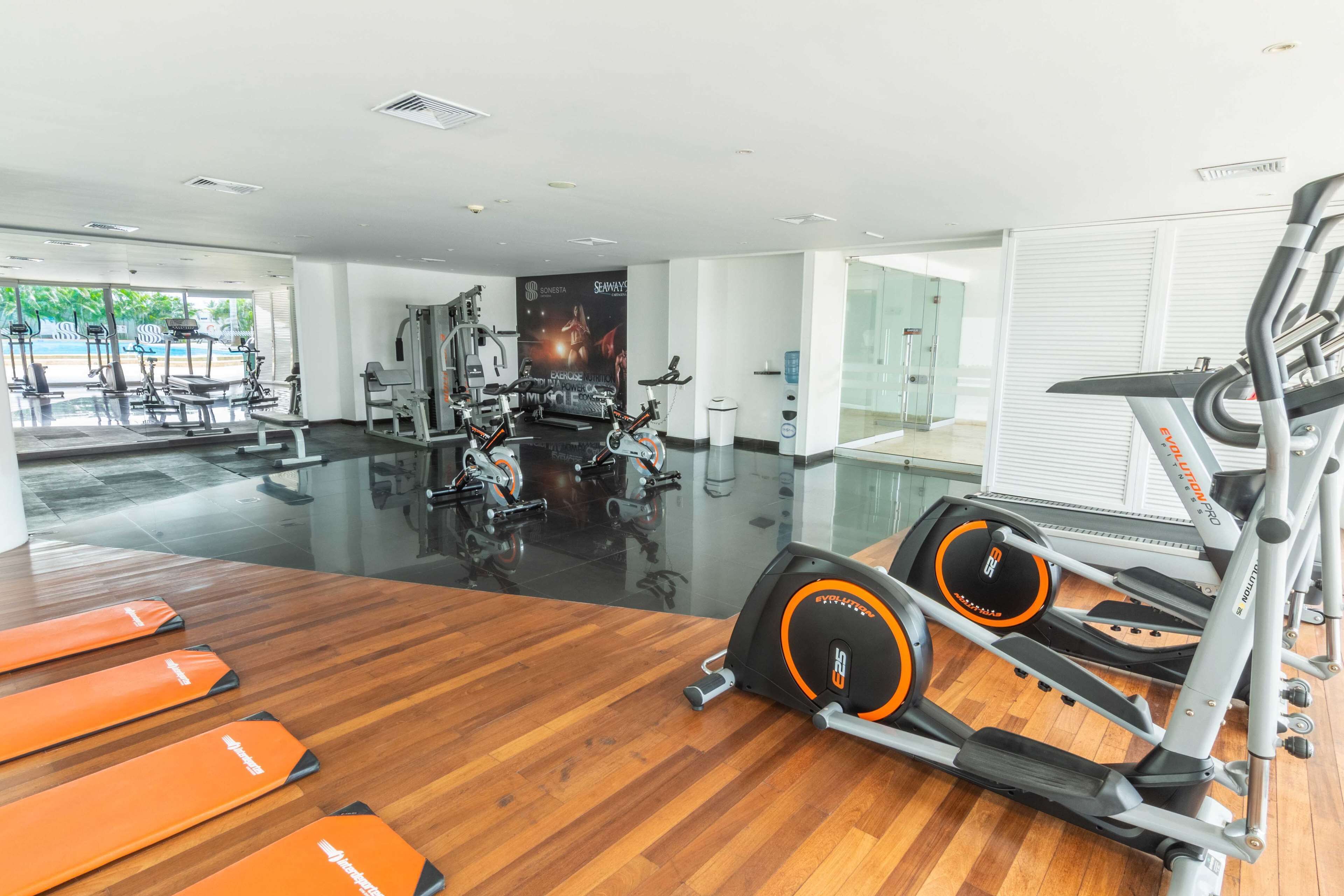 Ein Fitnessraum mit Trainingsgeräten, Holzboden und großen Fenstern.