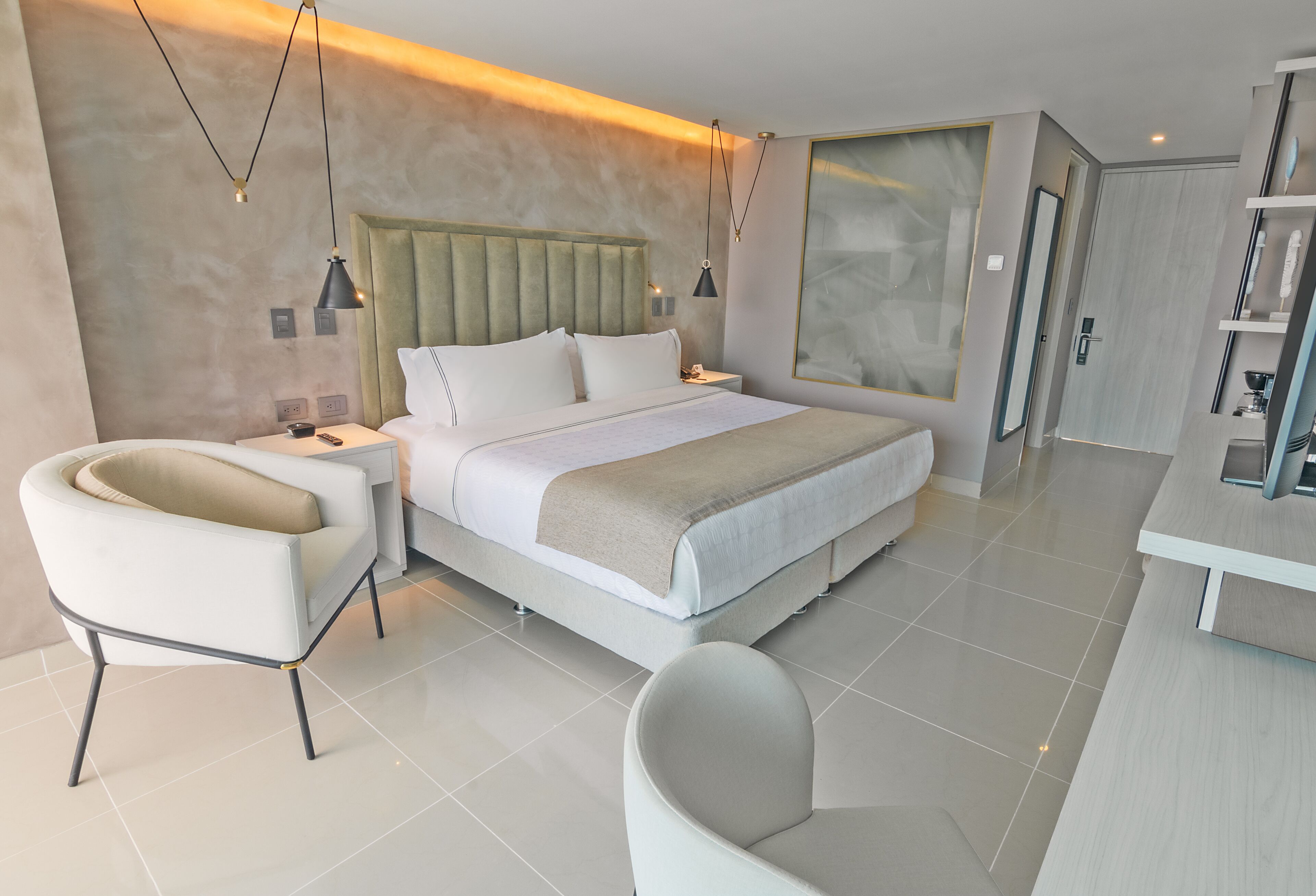 Una habitación de hotel moderna con una cama grande, una zona de estar con una silla, una mesita de noche y un ventanal amplio.