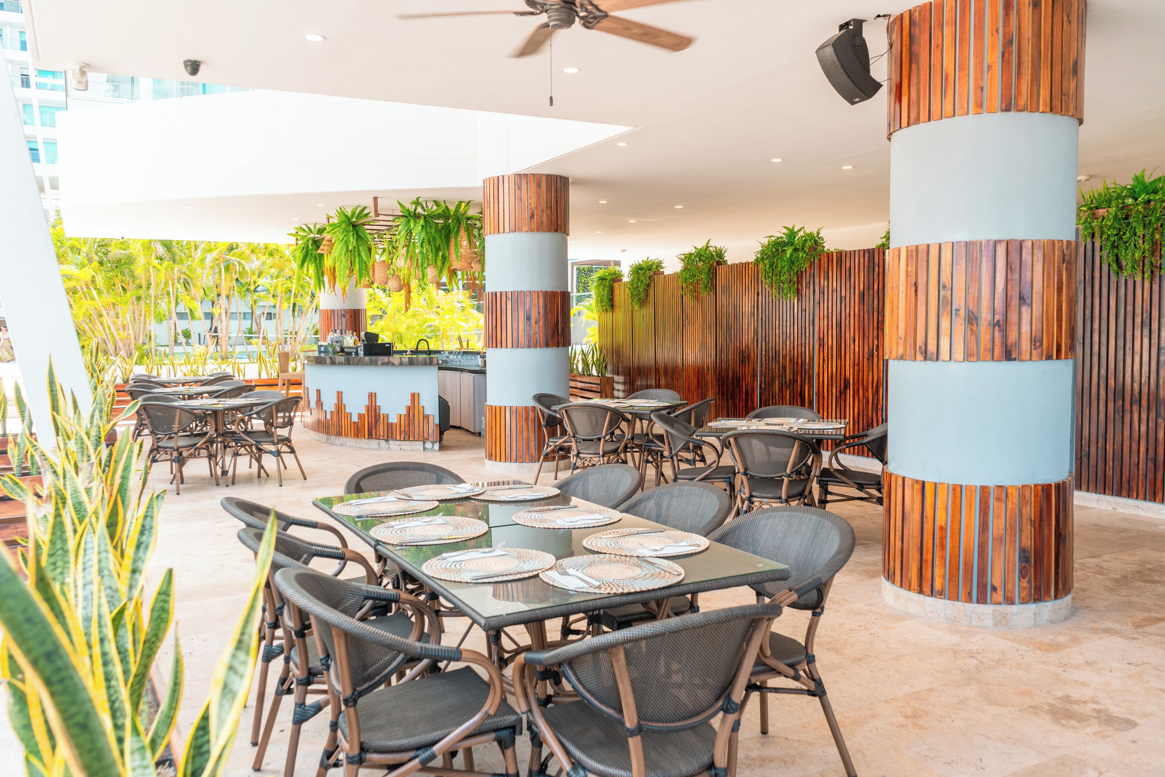 An outdoor dining area with round tables, wicker chairs, and vertical wooden panels.