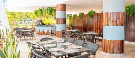 An outdoor dining area with round tables, wicker chairs, and vertical wooden panels.