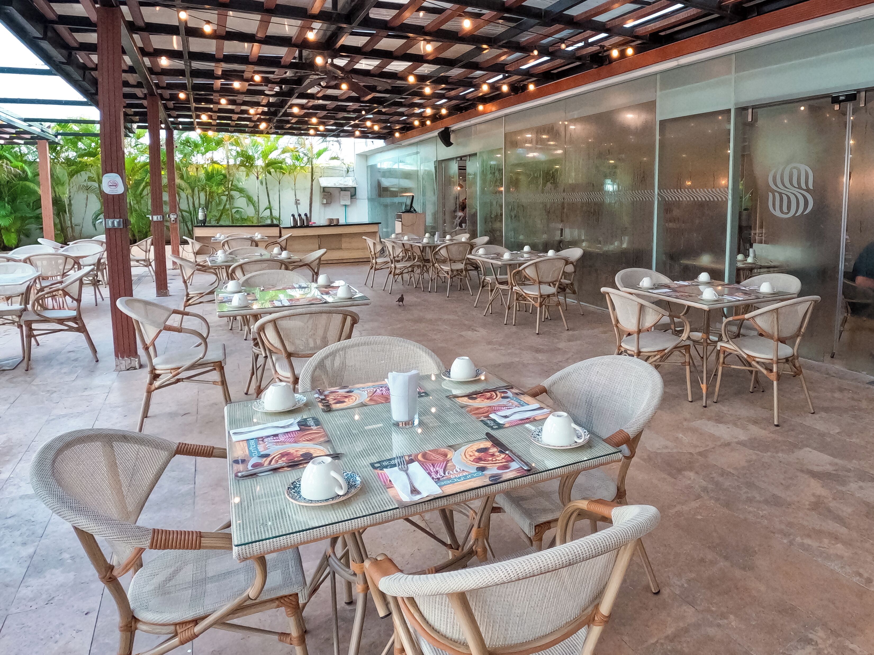 An outdoor dining area with wicker chairs and tables, some with menus and white teacups.