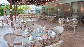 An outdoor dining area with wicker chairs and tables, some with menus and white teacups.
