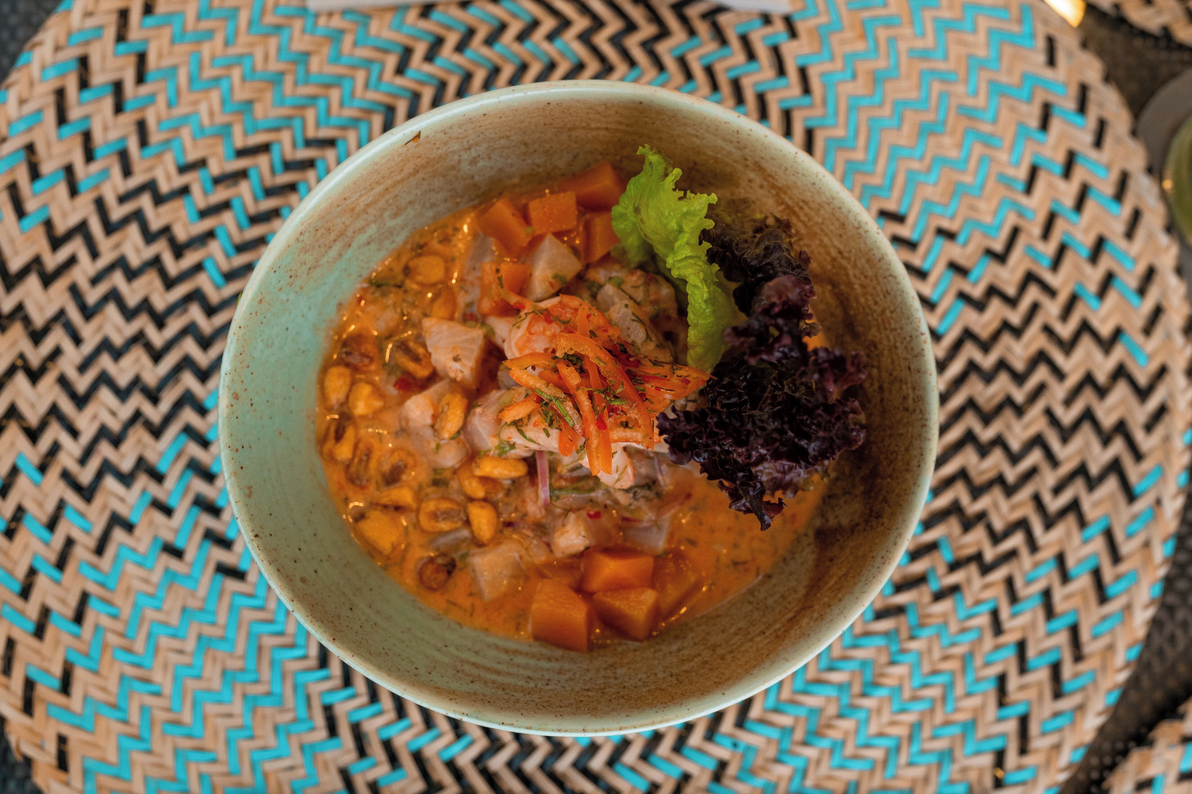 Un tazón de sopa con vegetales y carne, sobre un tapete tejido.