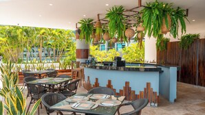 Un espace de restauration en plein air avec des tables et des chaises, un comptoir de bar et des plantes suspendues.