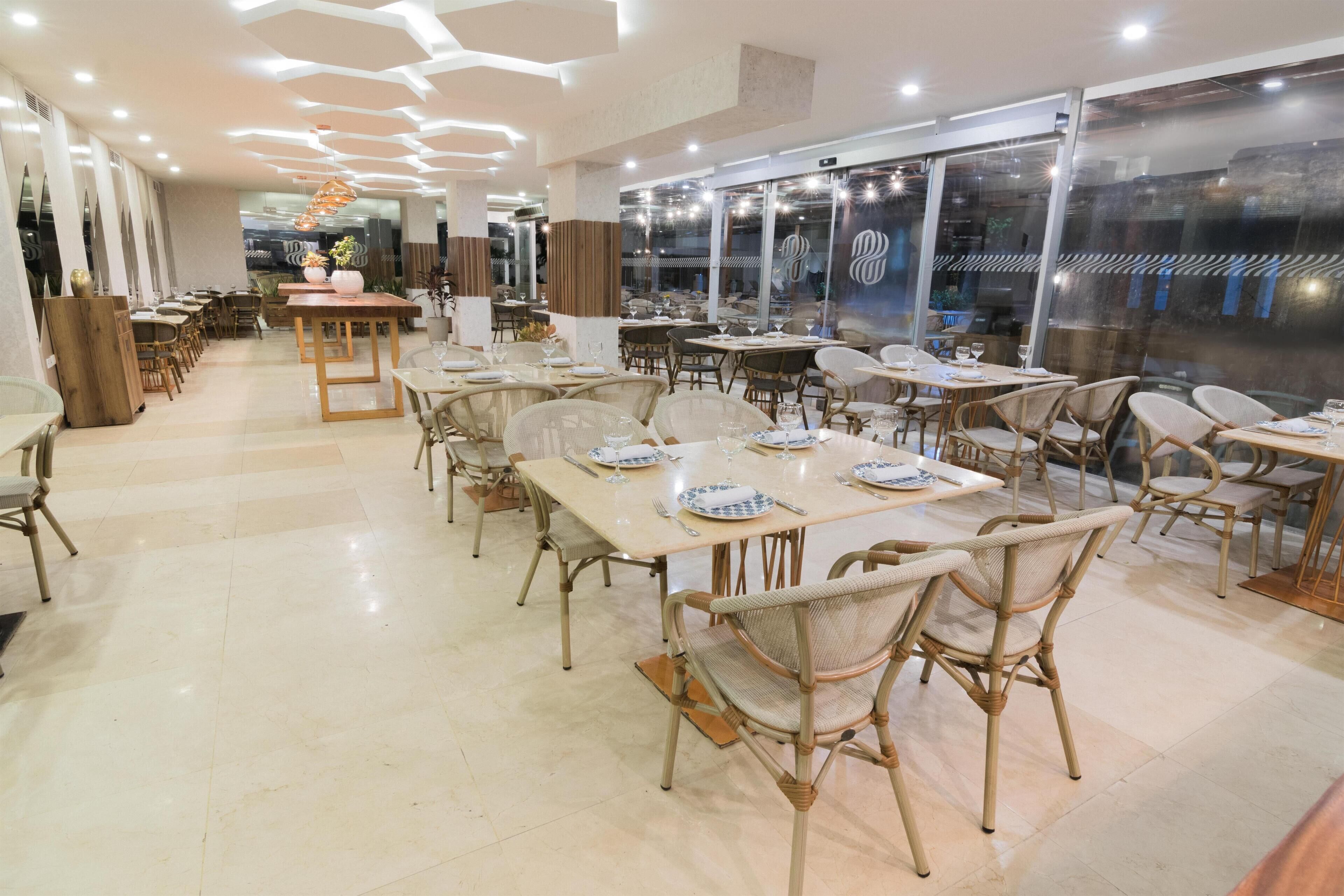 Un restaurante amplio con numerosas mesas y sillas, ventanas grandes y un diseño de techo moderno.