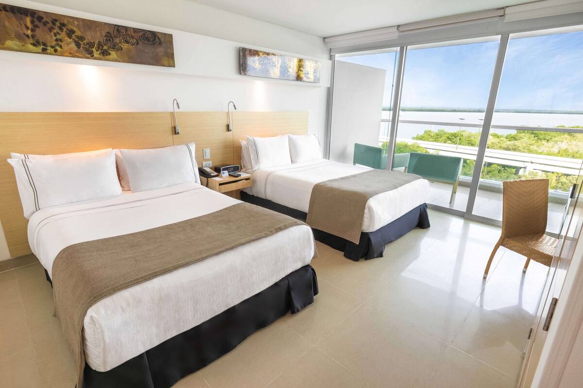 A hotel room with two beds, a balcony with a view, and a chair.