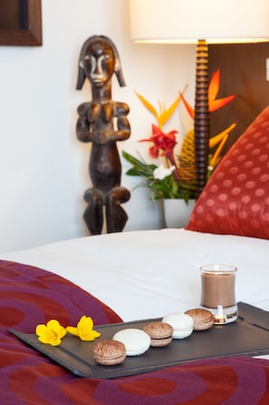 Una cama con una bandeja de macarons y una vela, un adorno de pared y una planta con flores rojas.