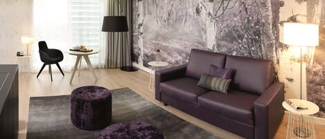 A modern living room with a purple sofa, two purple ottomans, a round coffee table, and a large wall mural.