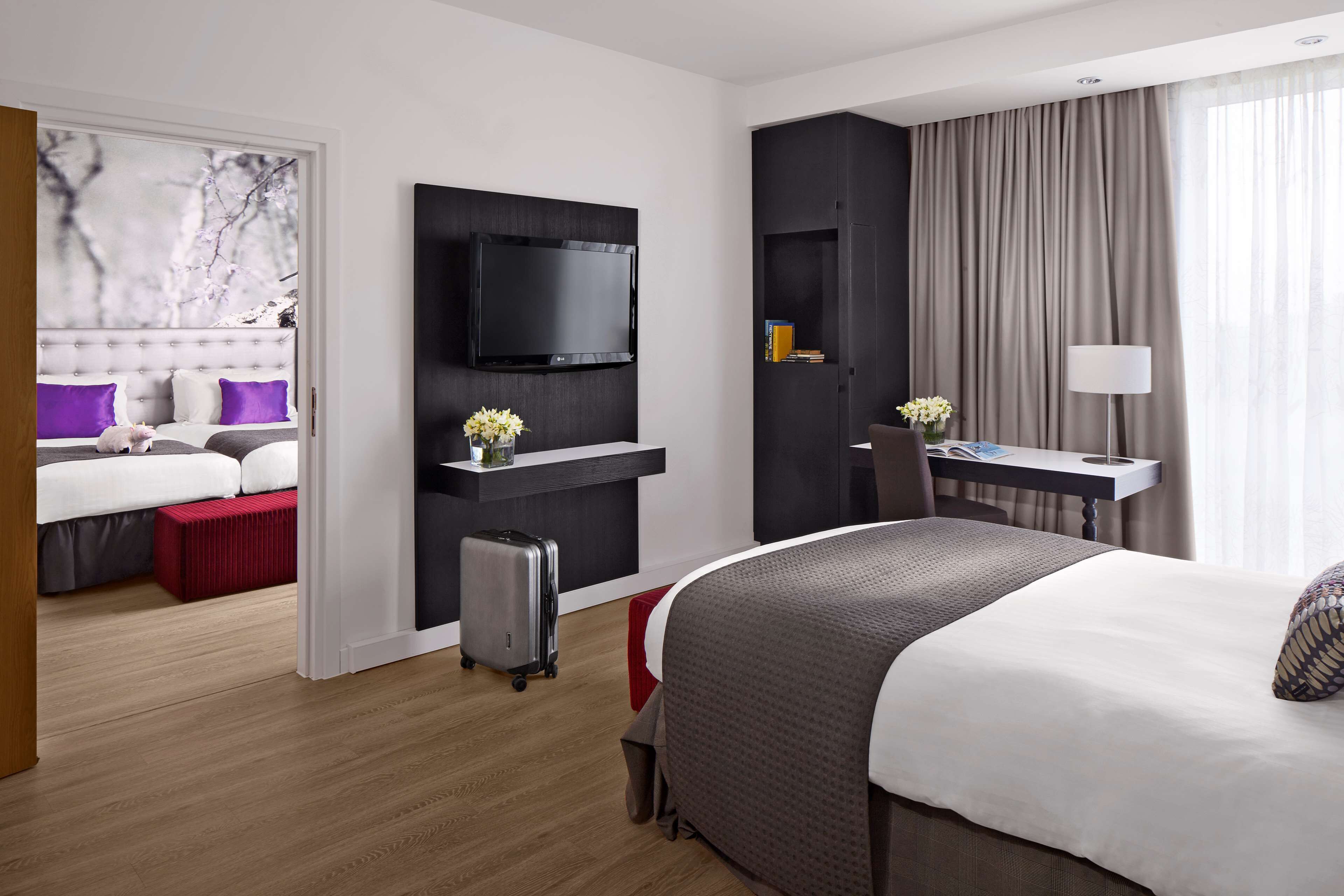 A modern hotel room with a large bed, a desk with a chair, a television, and a desk lamp.
