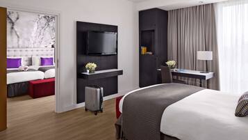 A modern hotel room with a large bed, a desk with a chair, a television, and a desk lamp.