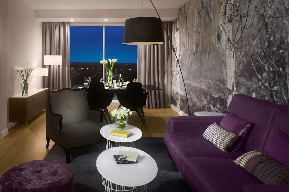 A modern living room with a dining area, a purple sofa, a white coffee table, and a view of the city at night.