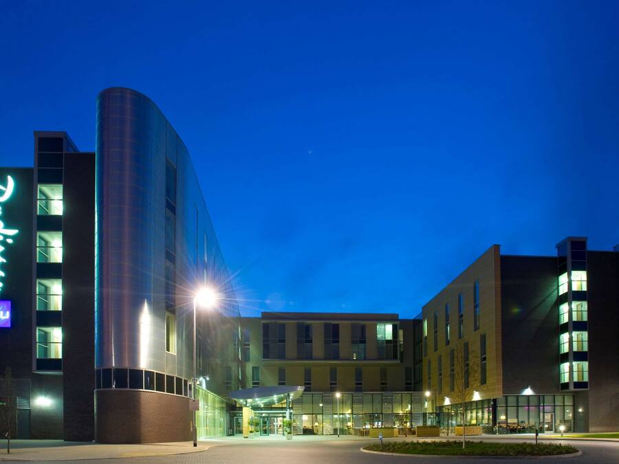 A modern hotel with a curved glass facade, a prominent neon sign, and a well-lit entrance area.