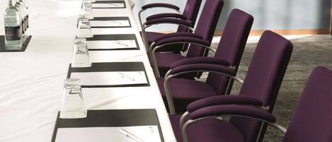 A conference room with a long table, purple chairs, and water bottles.