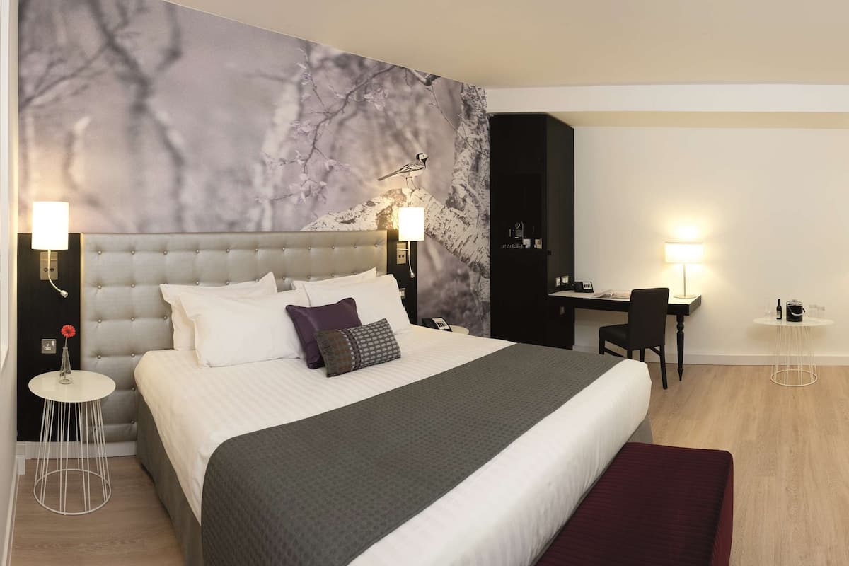 A modern hotel room with a large bed, a desk, and a TV.