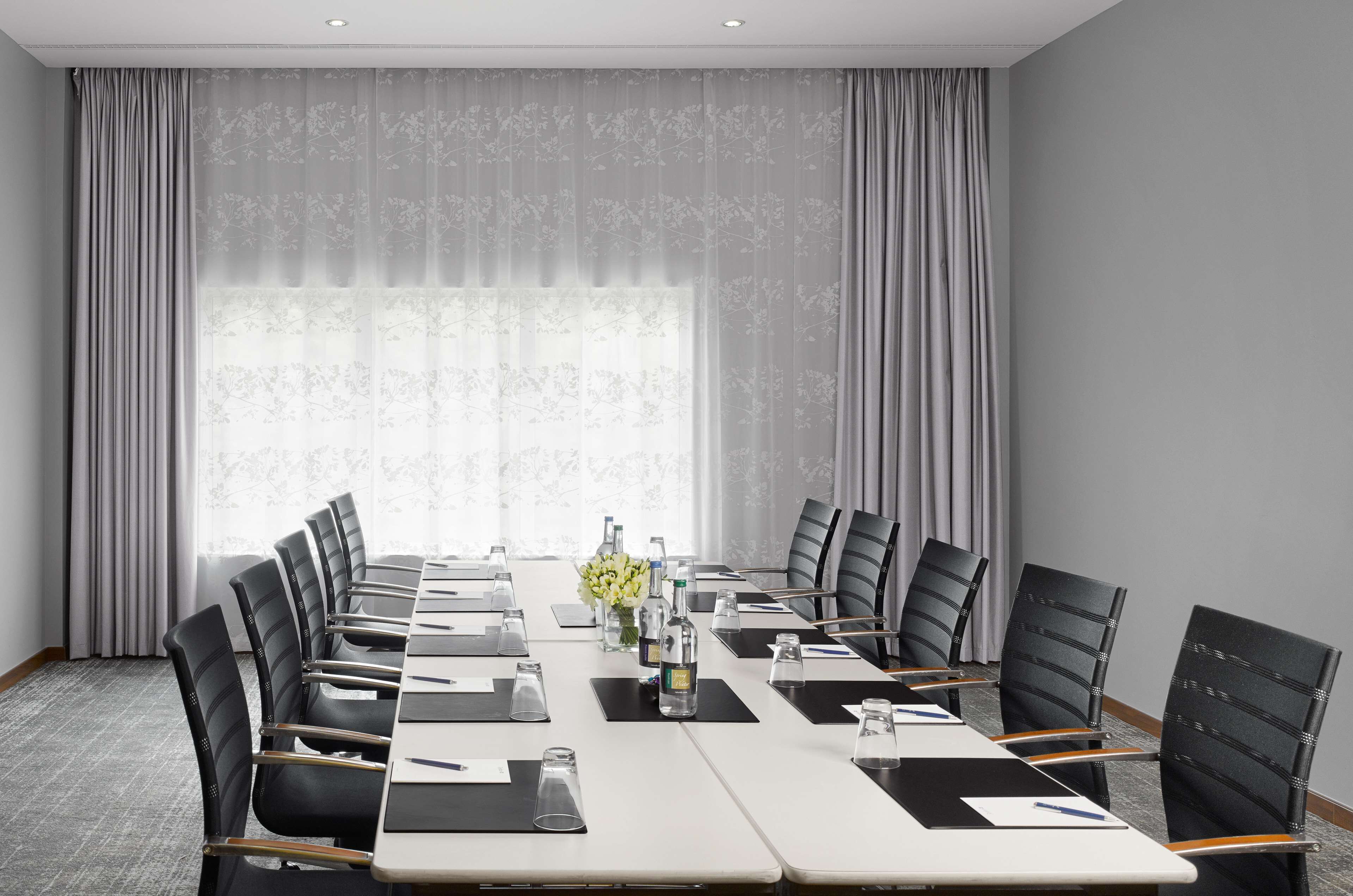 A conference room with a long table, black chairs, and a floral curtain backdrop.