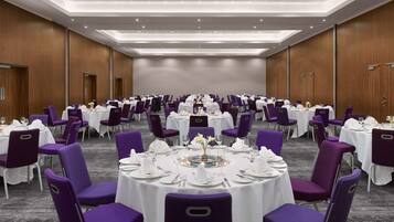 Un salón de conferencias con mesas redondas, sillas moradas y manteles blancos.