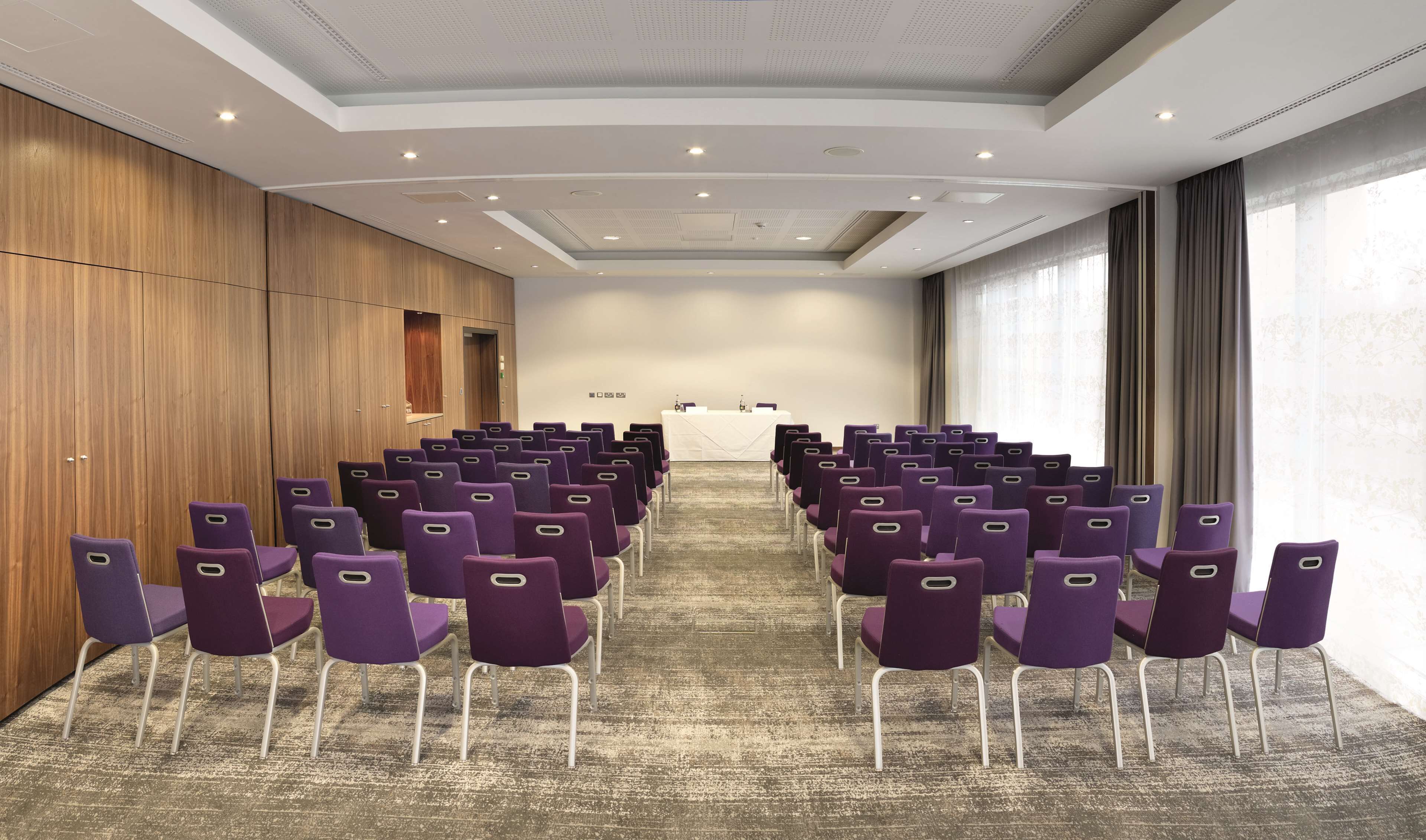 Une salle de conférence avec des rangées de chaises violettes disposées face à une table blanche sur laquelle se trouve un pupitre.