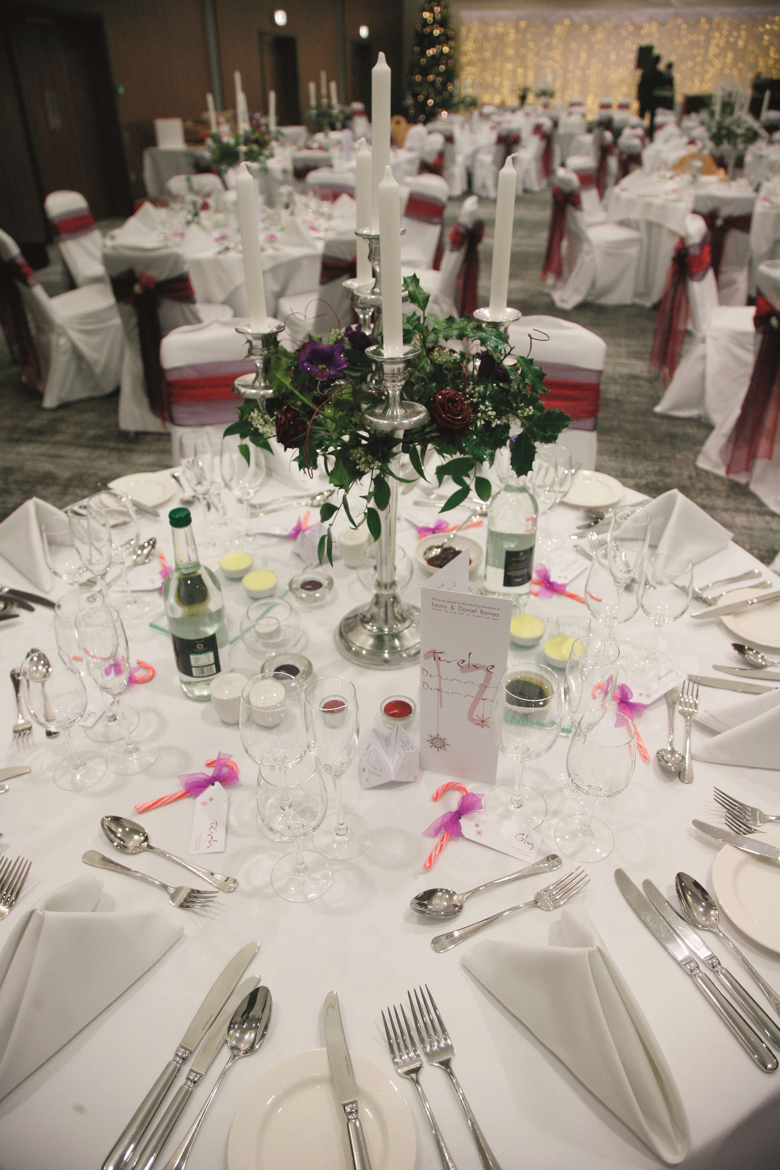 A banquet hall with round tables set for a formal event, featuring white tablecloths, silverware, and candles.