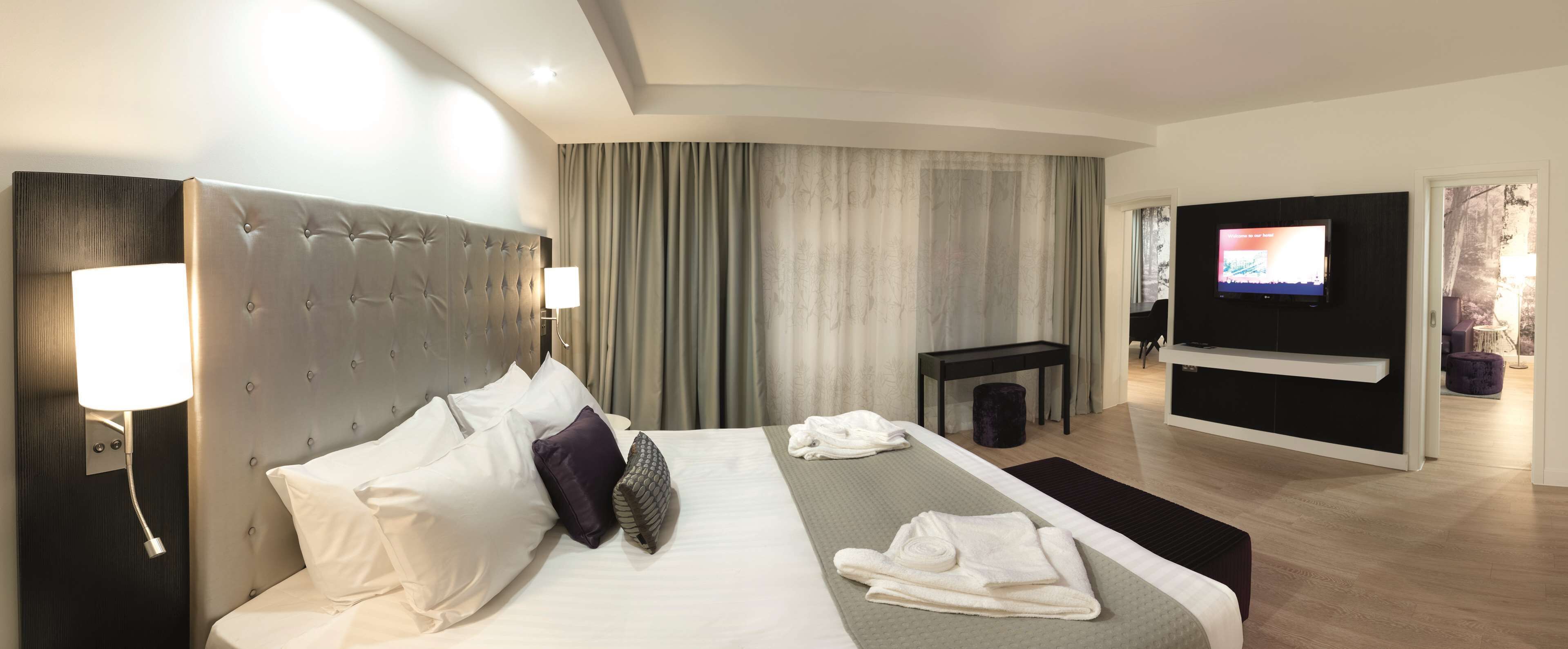 Una habitación de hotel moderna con una cama grande, un televisor de pantalla plana y una zona de estar con televisor.