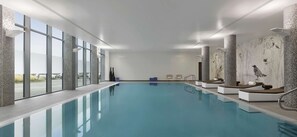 An indoor swimming pool with clear glass walls, a tiled floor, and a view of the outside.