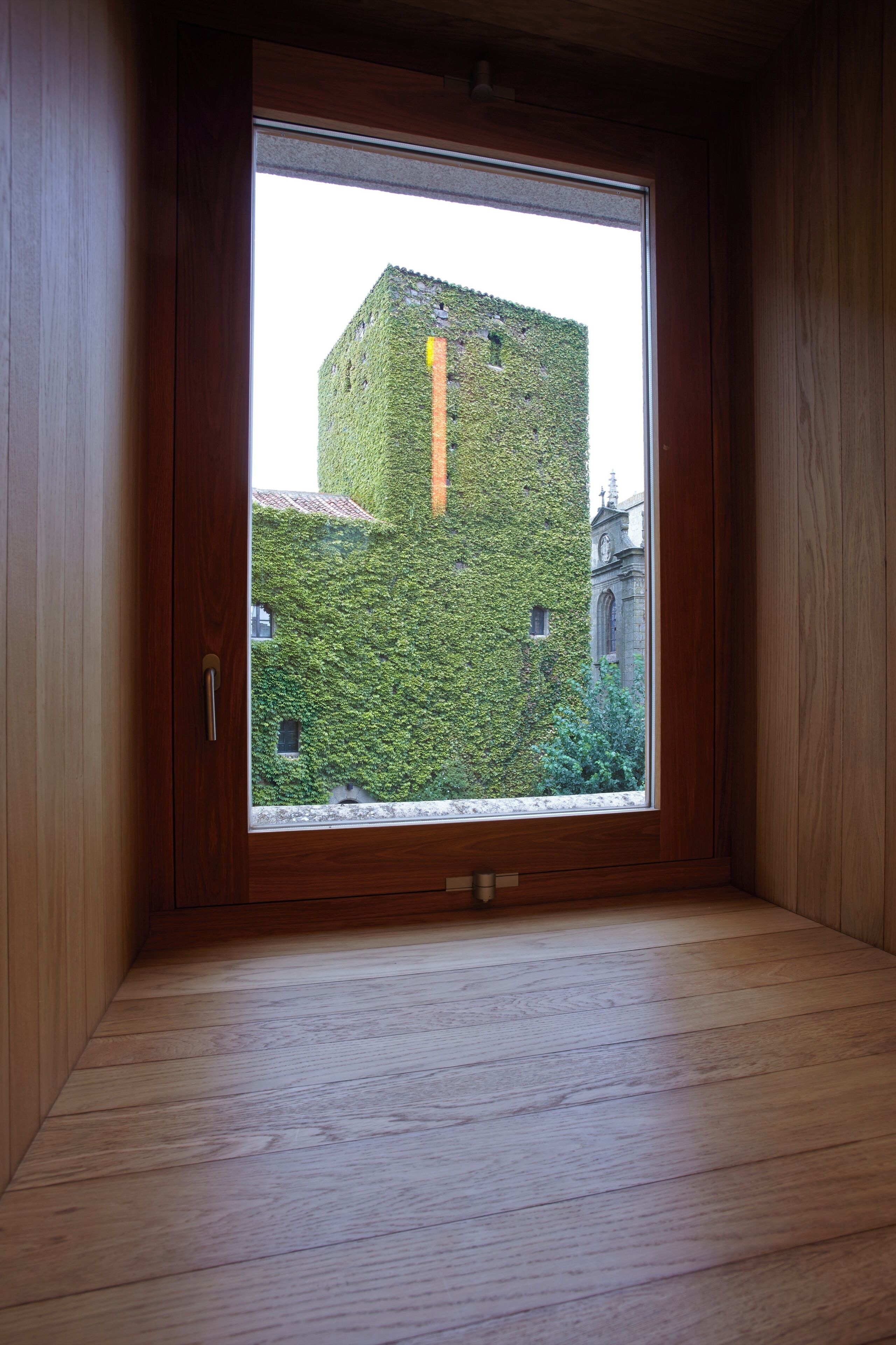 Una habitación con un ventanal grande, paredes de madera y vistas a un edificio cubierto de hiedra.