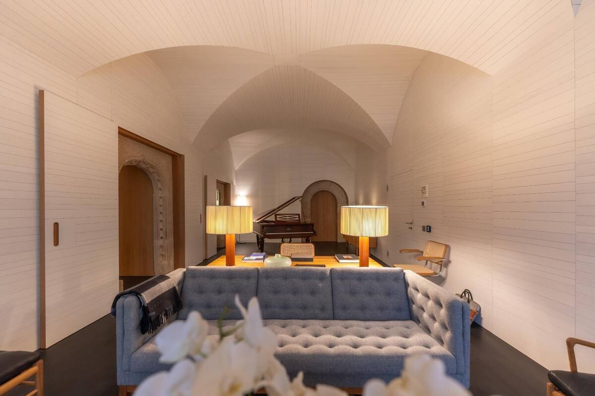A room with a sofa, two lamps, a piano, and a chair.