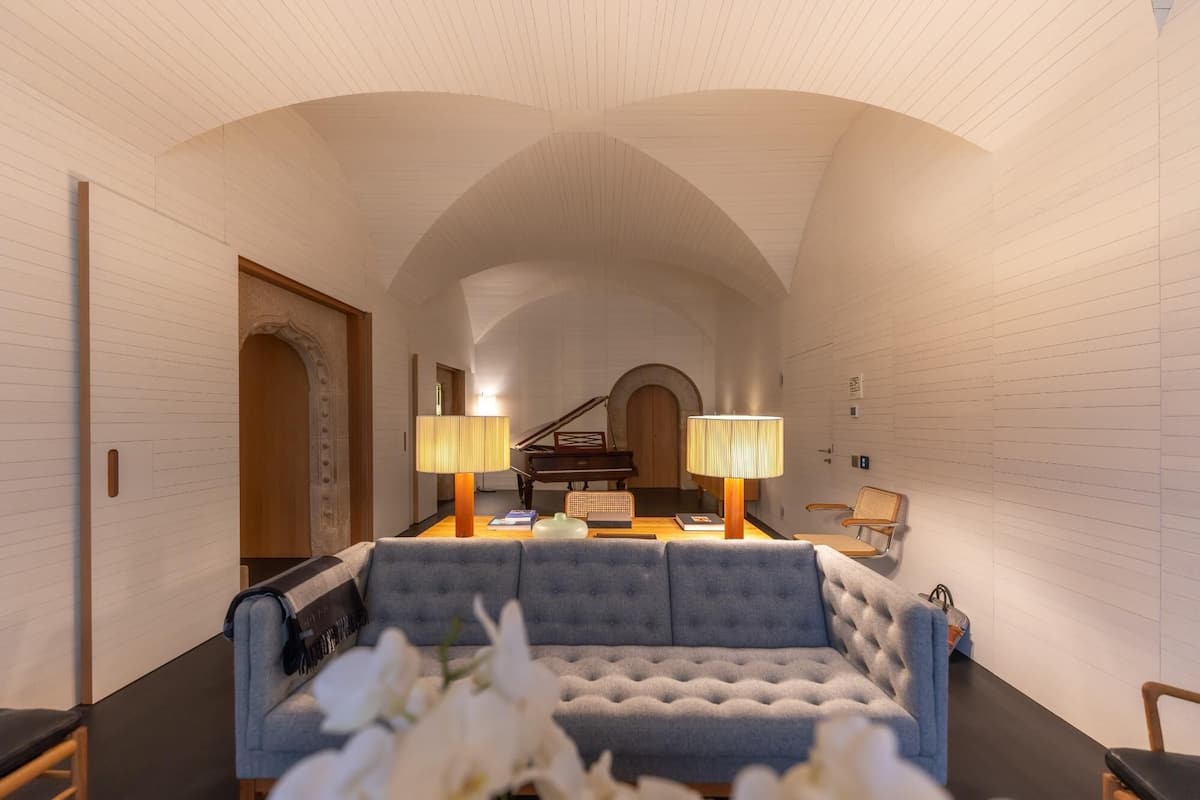 A room with a sofa, two lamps, a piano, and a chair.