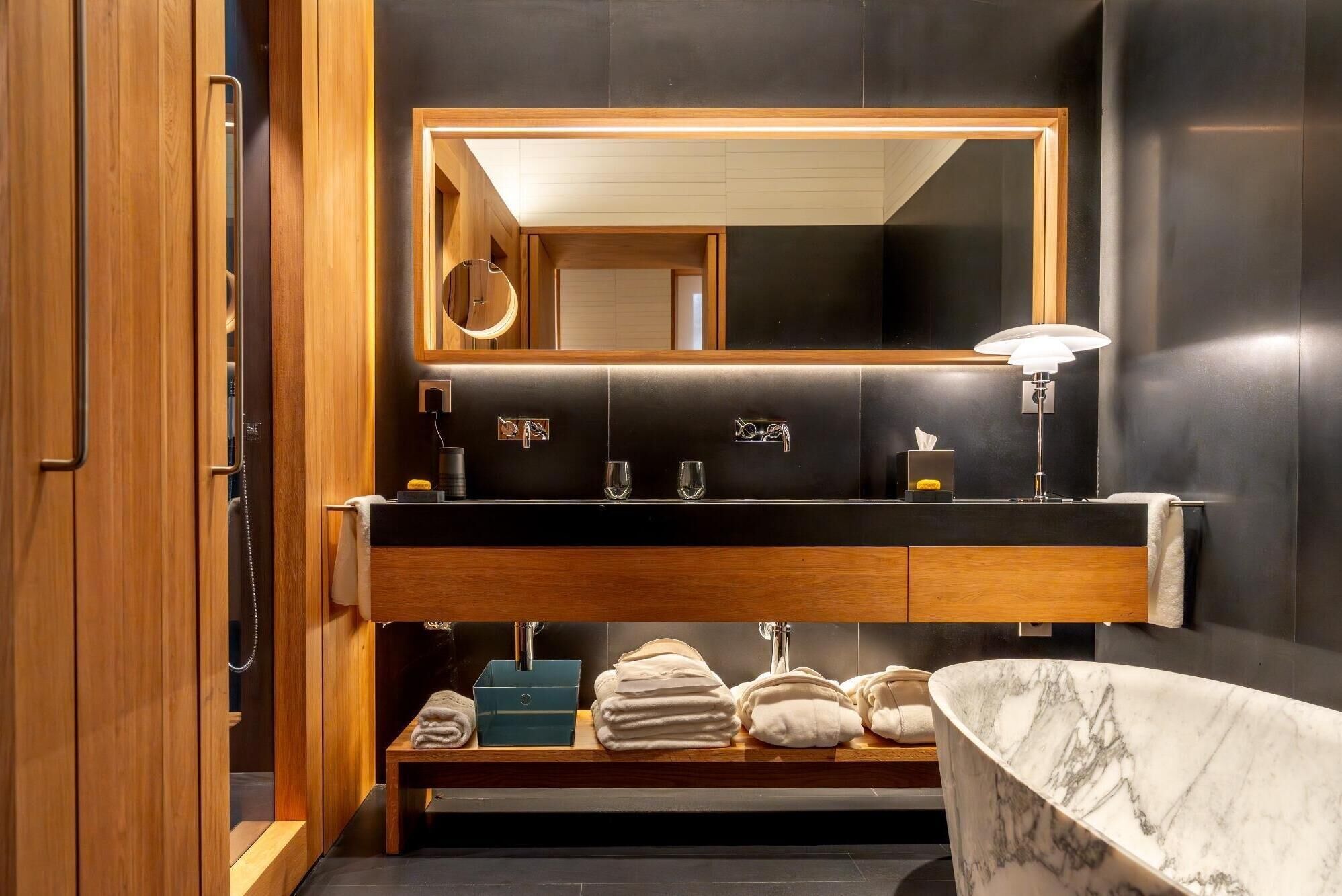 Un baño moderno con tocador de madera, un espejo grande, lavabo de mármol y una bañera independiente.