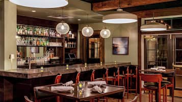 A bar area with a long counter, multiple hanging light fixtures, and a variety of bottles and glasses on shelves.