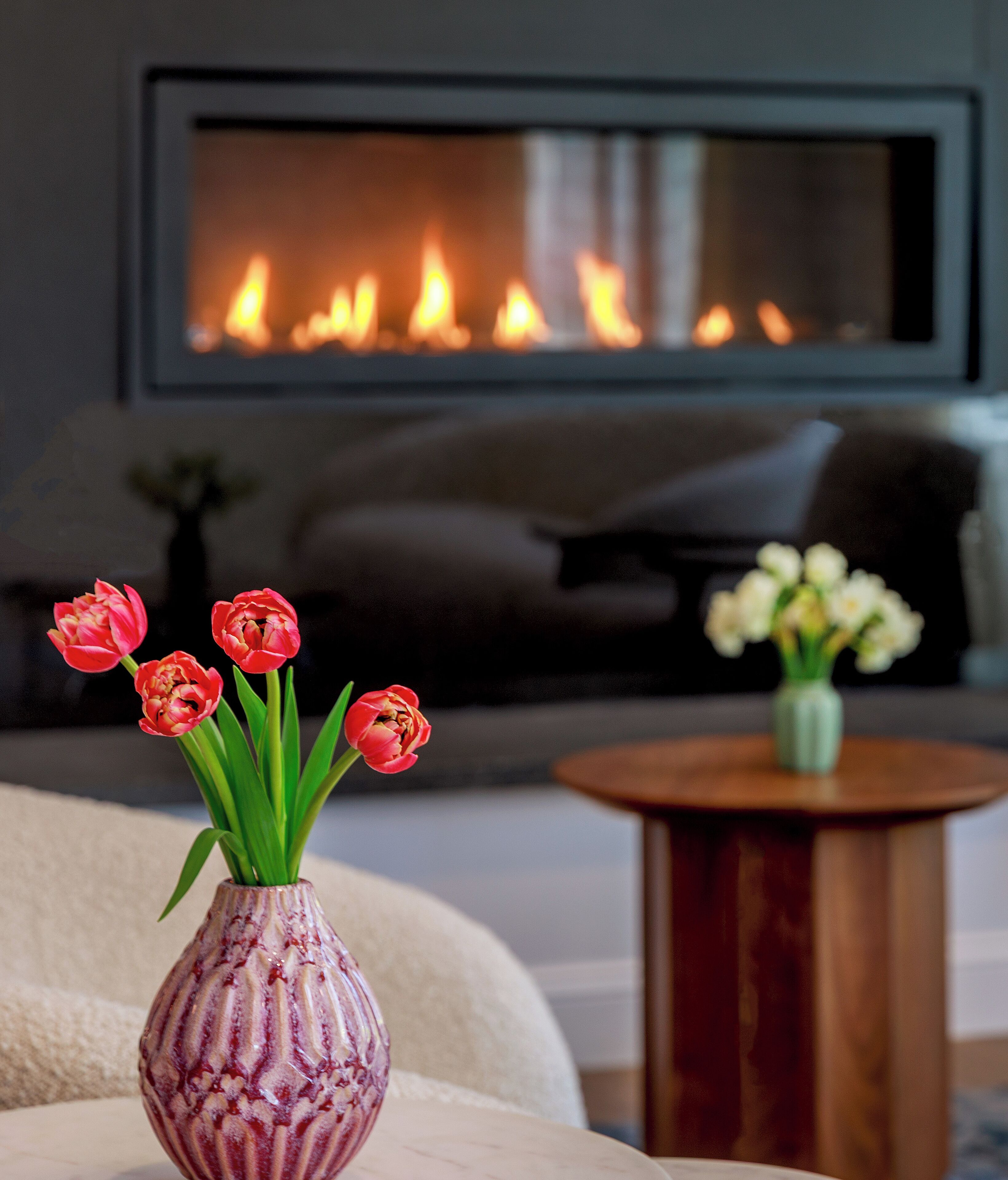 Un salon avec une cheminée, un canapé et deux vases de fleurs.