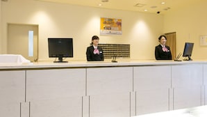 Een receptiebalie met twee medewerkers, een computer monitor en een ingelijst certificaat aan de muur.