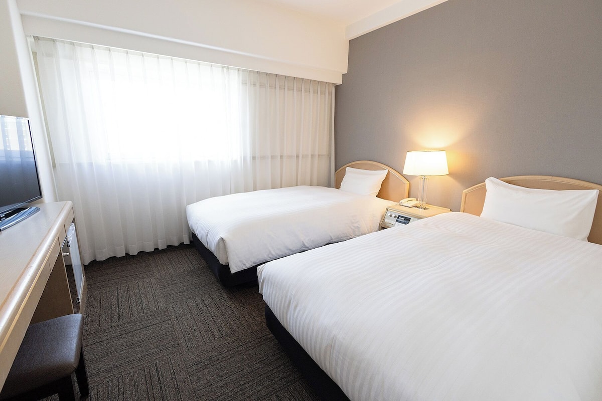 Une chambre d’hôtel avec deux lits, un bureau, une télévision et une lampe.