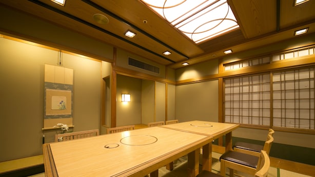 Een traditionele Japanse kamer met tatami vloerbedekking, een lange houten tafel en lage houten stoelen.