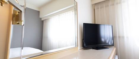 A hotel room with a bed, a television on a wooden dresser, a mirror, and a window with curtains.