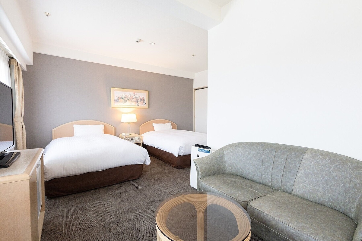 Une chambre d’hôtel avec deux lits, un canapé, une petite table et un téléviseur.