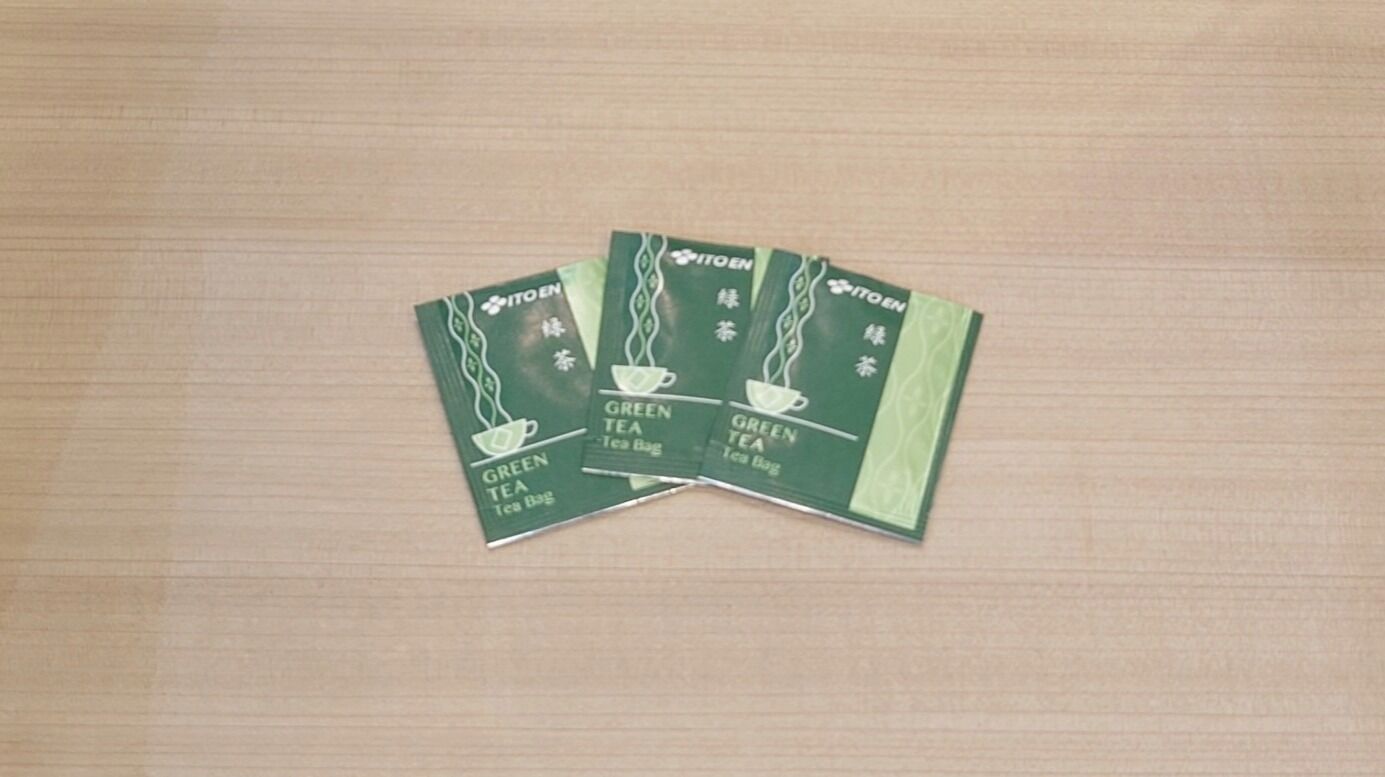 Three green tea bags on a wooden surface.