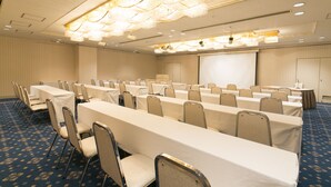 Un salón de conferencias con filas de mesas y sillas, una pantalla de proyector y una lámpara de araña grande.