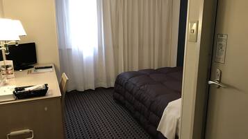 A hotel room with a bed, a desk with a lamp, a television, and a window with curtains.