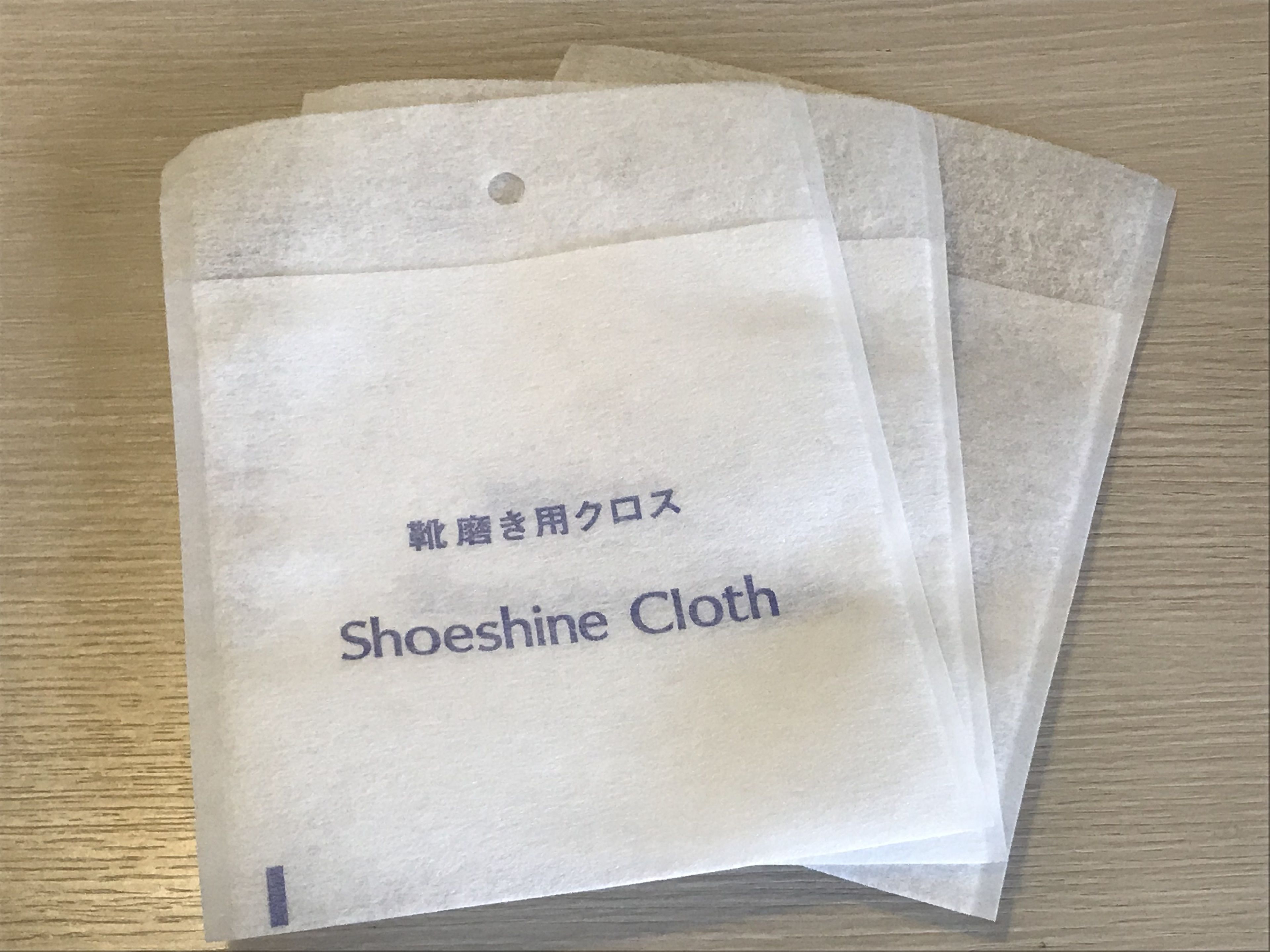 A pair of shoe cleaning cloths labeled "Shoeshine Cloth" on a wooden surface.