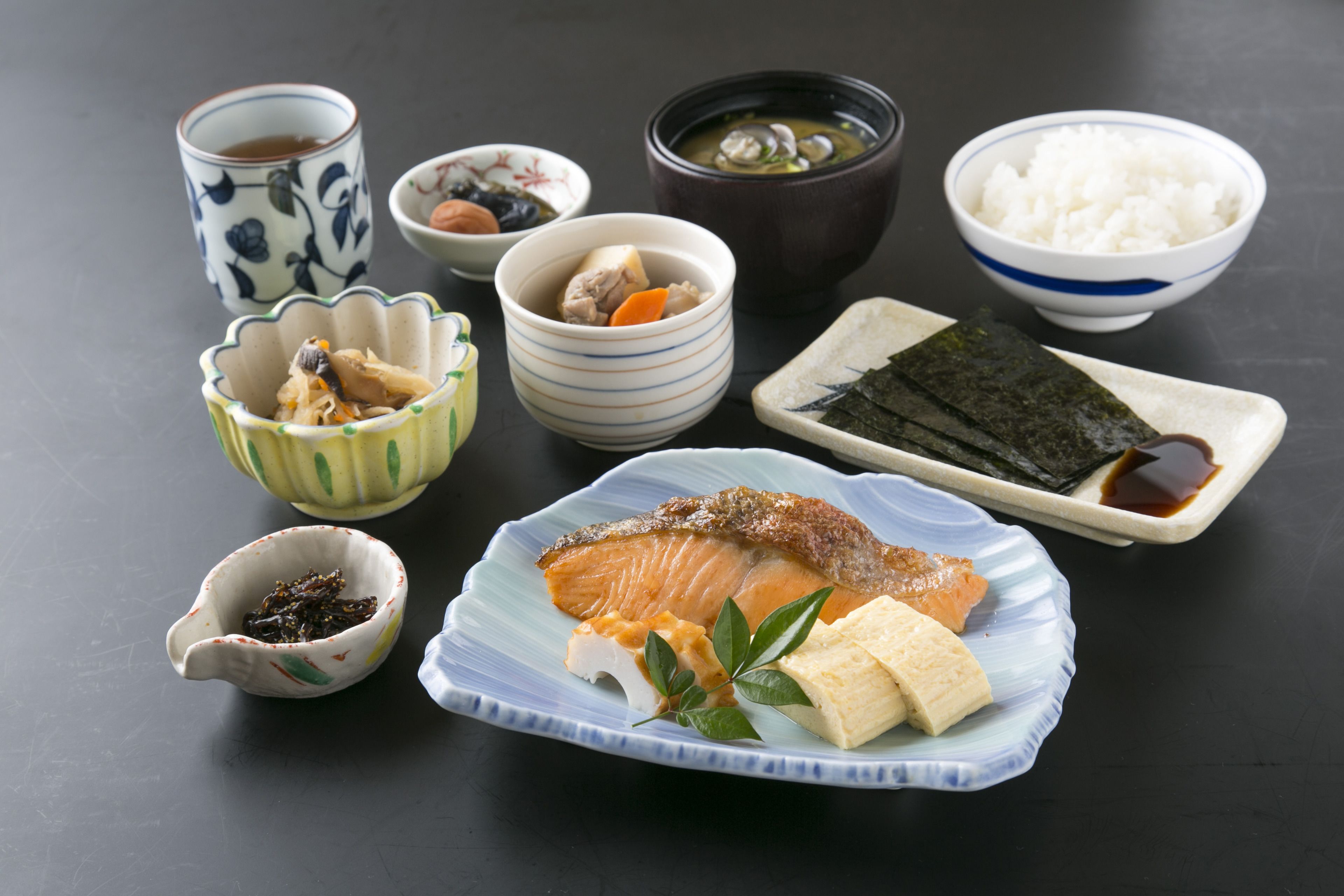 A variety of Japanese dishes including salmon, rice, and soup, served on a black table.