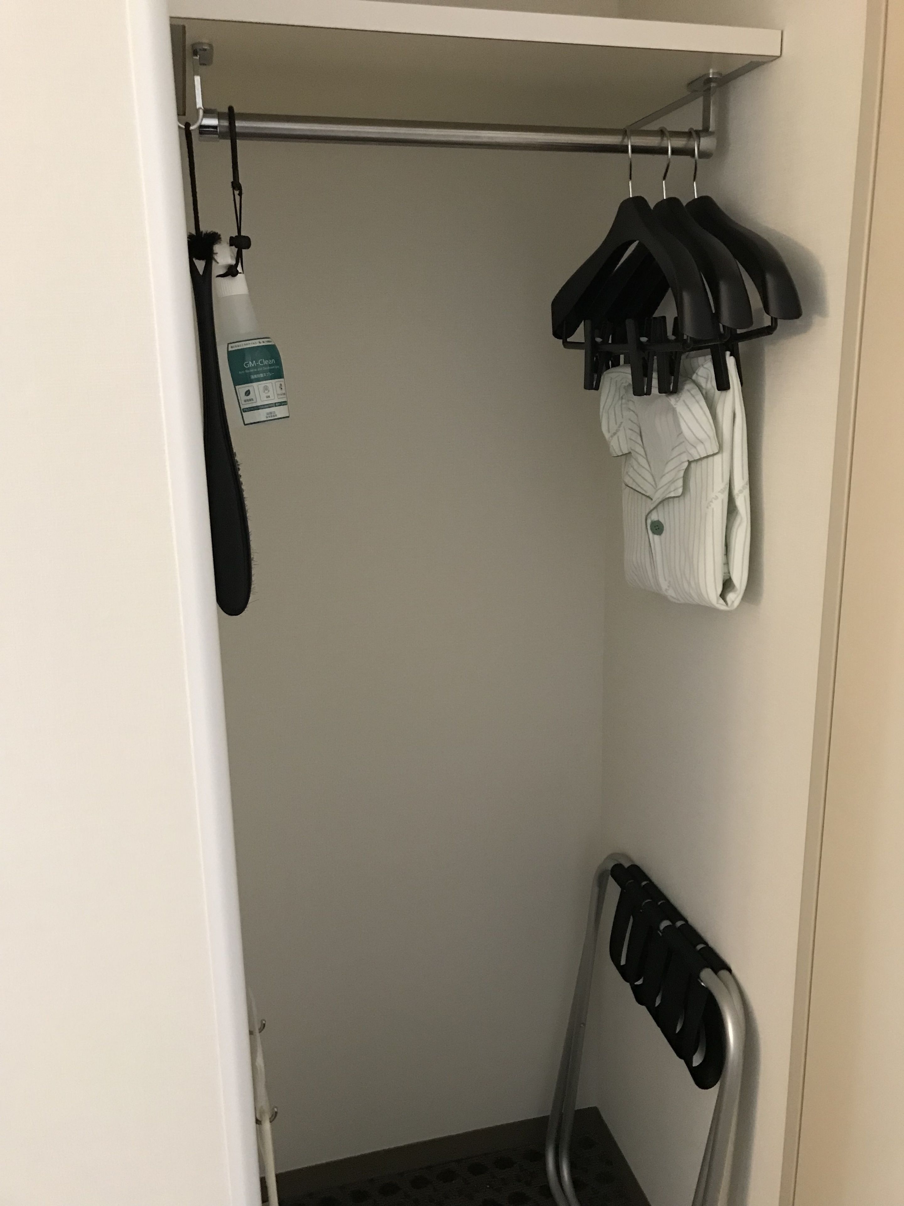 A closet with hanging clothes, a coat rack, and a cleaning spray bottle.