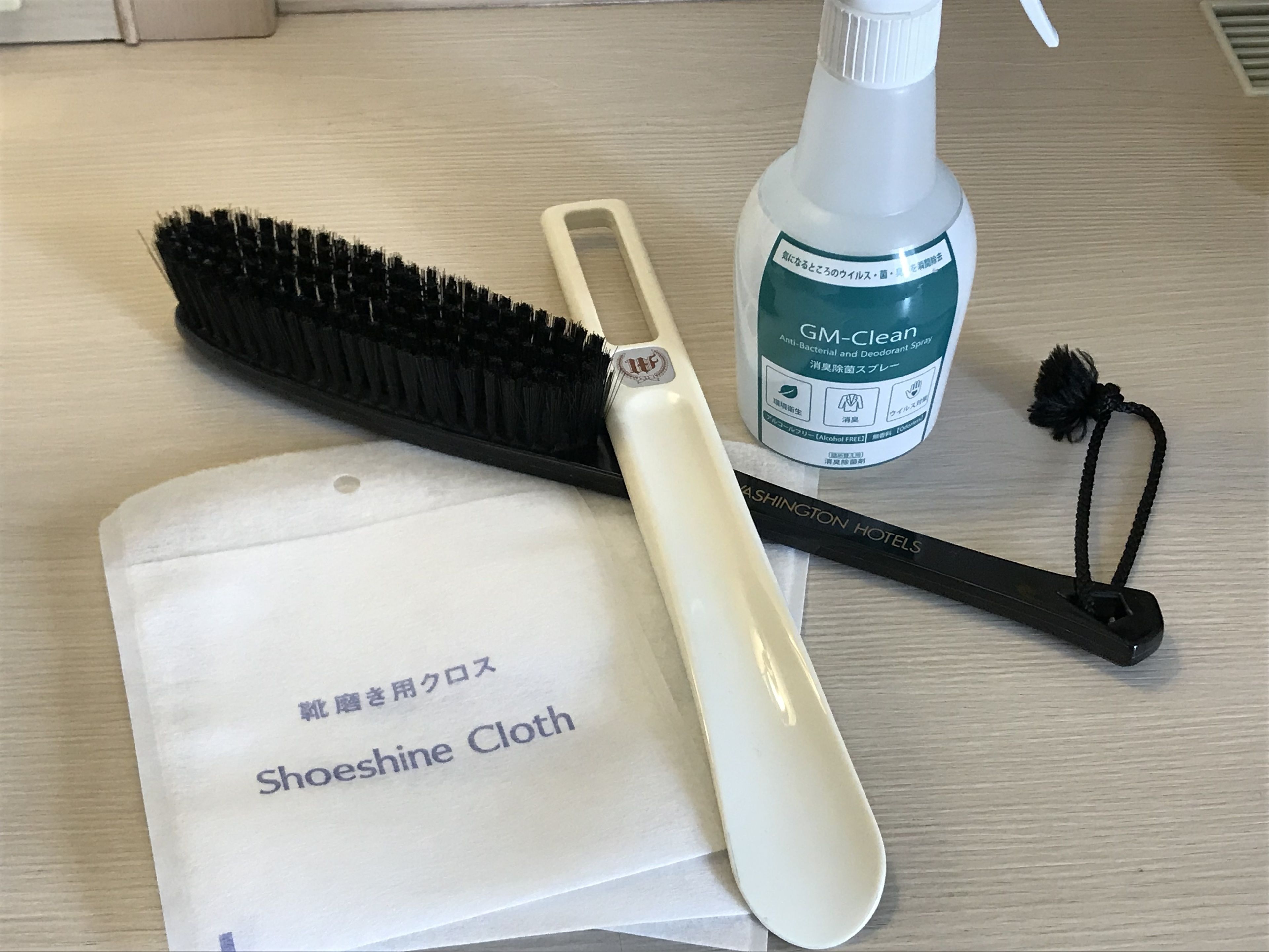 A bottle of GM-Clean, a black hairbrush, a white cleaning cloth, and a black comb on a wooden surface.