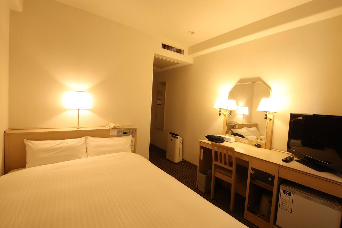 Een hotelkamer met een bed, bureau, televisie en twee lampen.