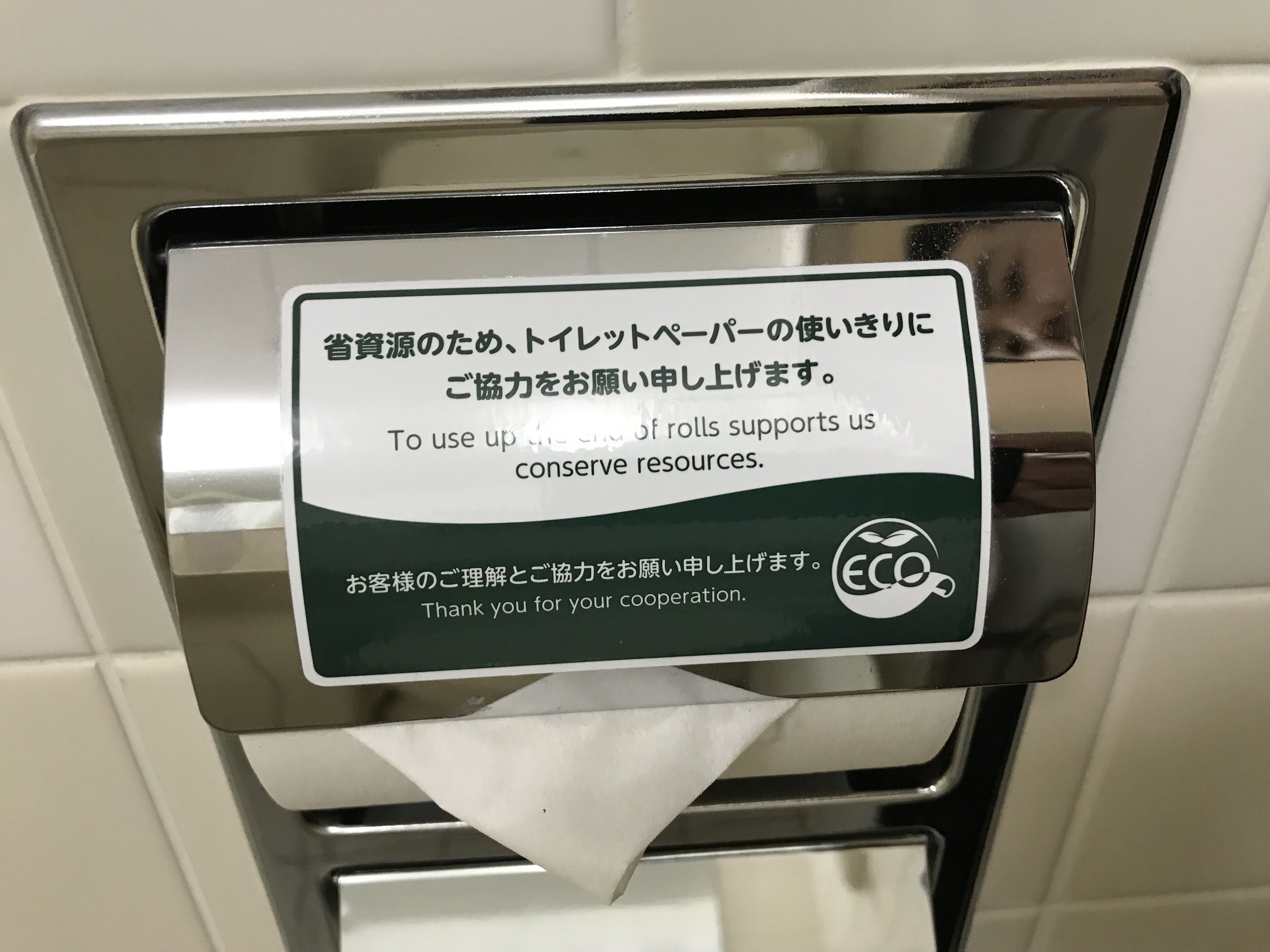 Letrero en un baño público que invita a usar toallas de papel para ahorrar recursos.