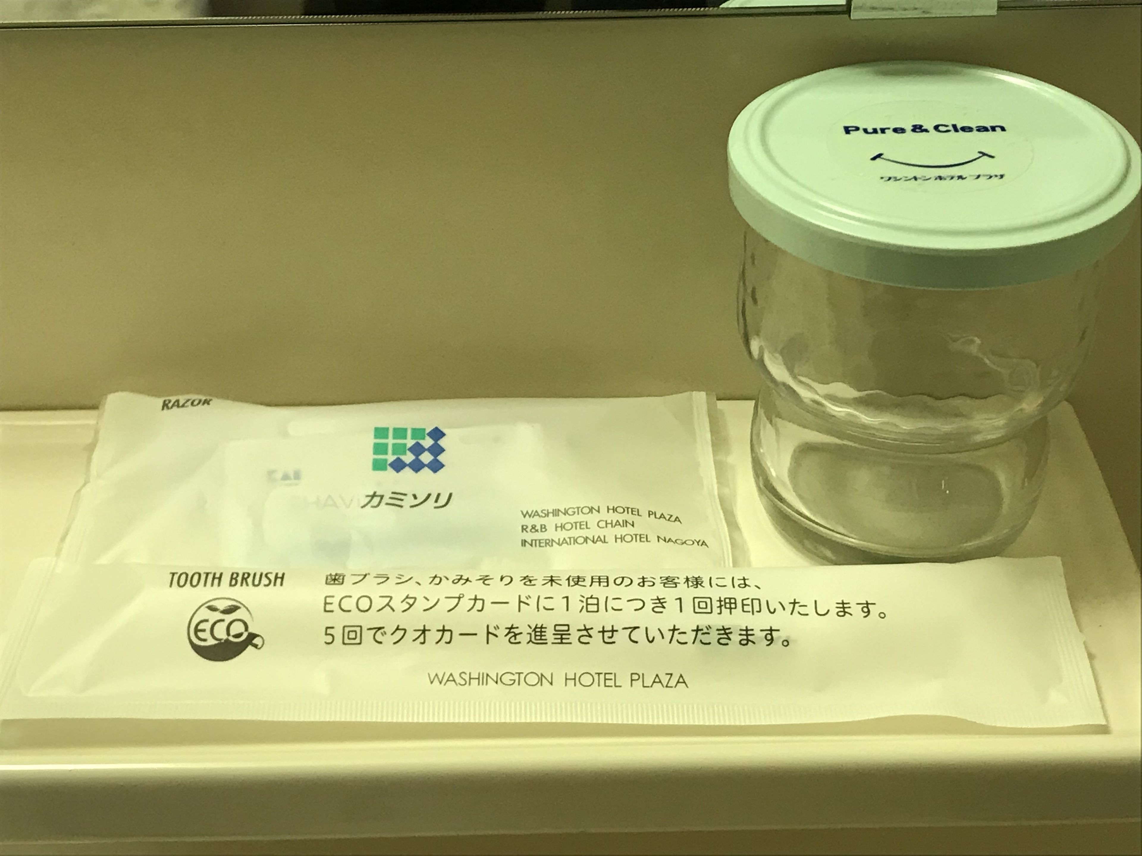 Un bicchiere con coperchio etichettato "Pure & Clean" e una bustina bianca con testo in giapponese e il logo del Washington Hotel Plaza.