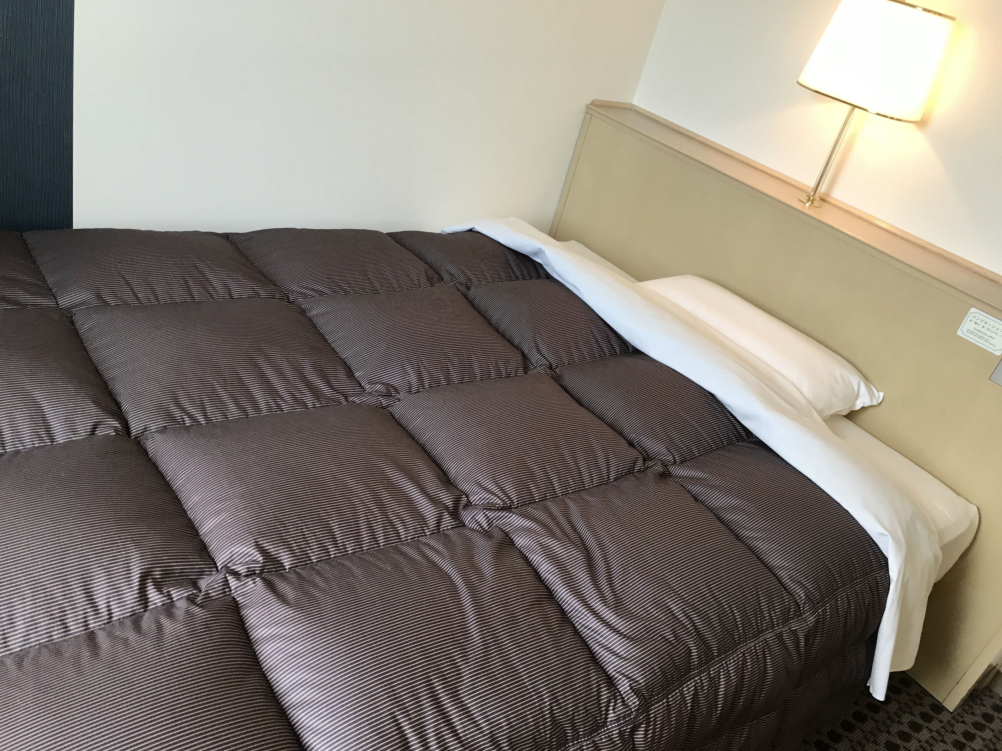 A neatly made bed with a striped comforter and a white pillow.