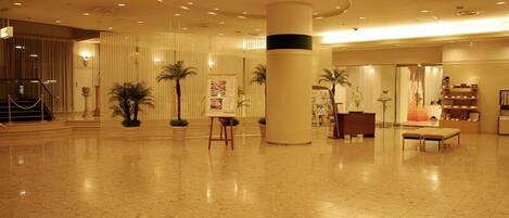 Een ruime lobby met een gepolijste marmeren vloer, een centrale kolom en een receptiebalie.