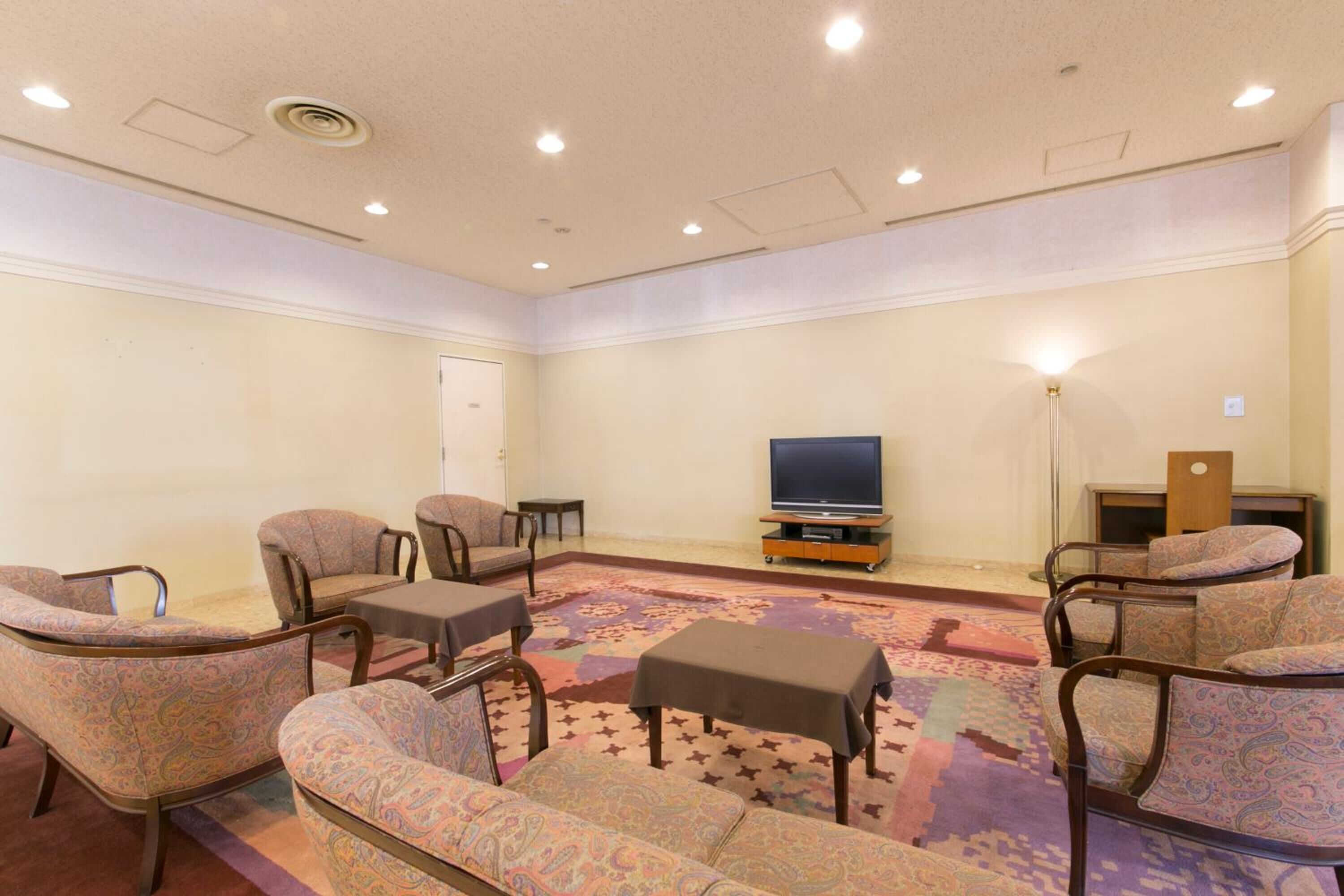 Una habitación con sillones estampados, una mesita y un televisor sobre un mueble.
