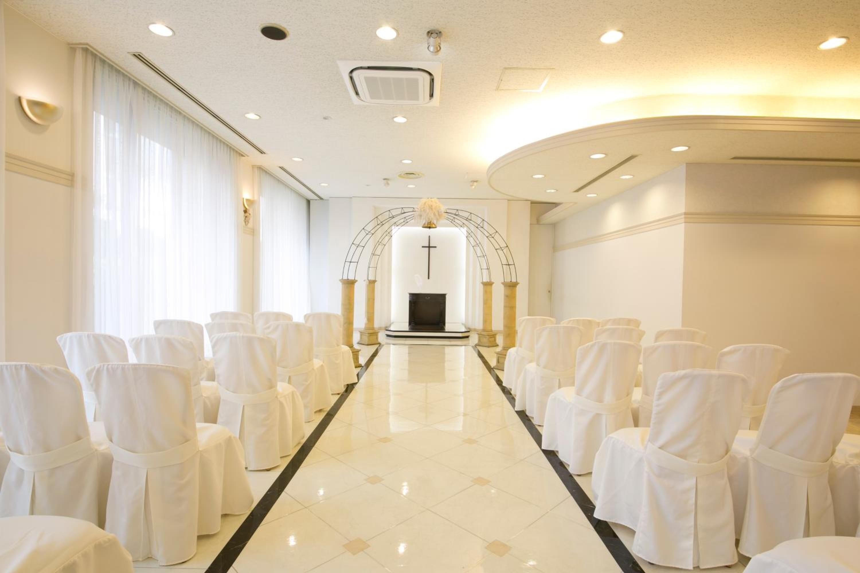 A church interior with rows of white chairs, a central aisle, and a cross at the front.