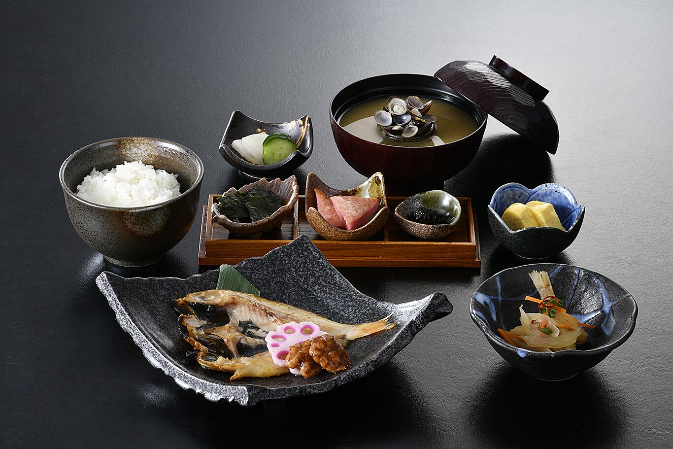 Un montaje tradicional de comida japonesa con diferentes platos, incluyendo arroz, pescado y sopa.
